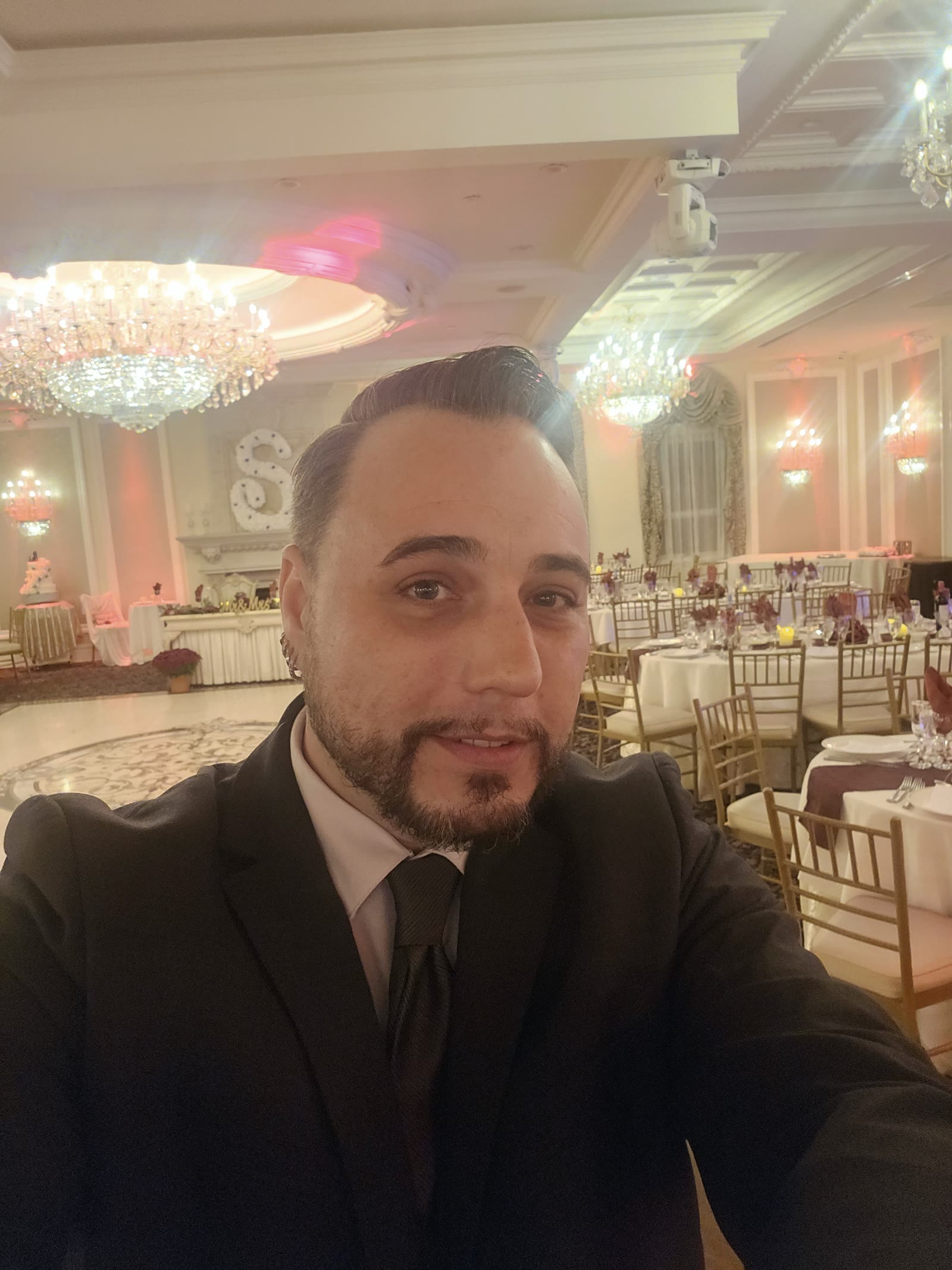Barry Proud in a black suit and tie at a chandelier-lit wedding reception